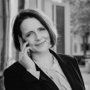 Eine Frau mit Kurzhaarfrisur spricht am Telefon und lächelt freundlich.